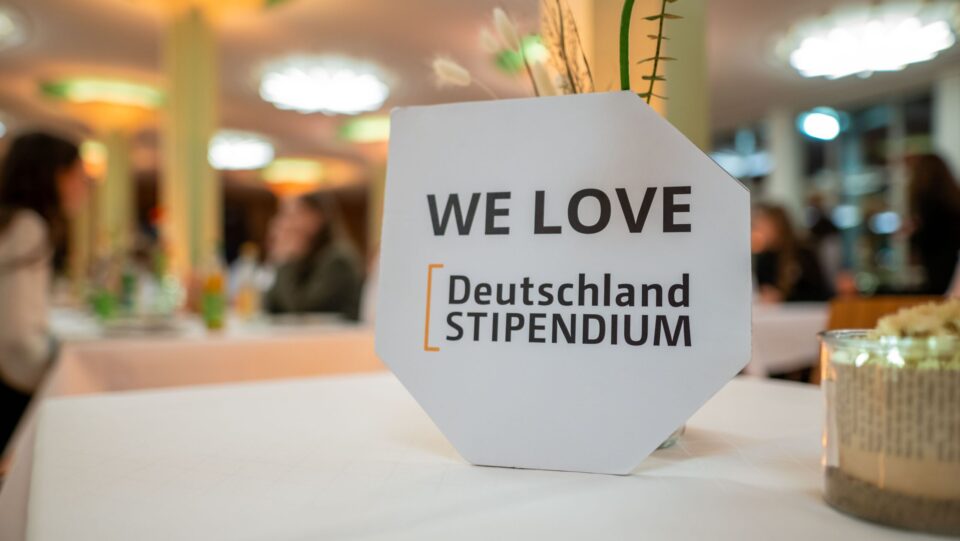 Auf einer weißen Tischdecke steht ein Schild mit der Aufschrift: We Love Deutschlandstipendium